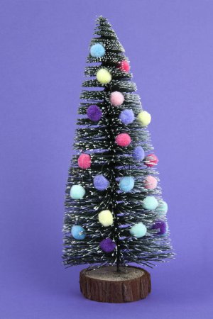 Photo for Miniature christmas tree decorated with mini garlands and pompoms as baubles. Violet background. Minimal still life photography - Royalty Free Image