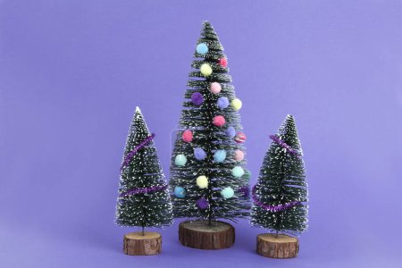 Photo for Miniature christmas tree decorated with mini garlands and pompoms as baubles. Violet background. Minimal still life photography - Royalty Free Image