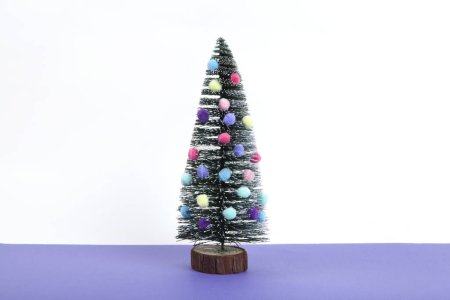 Photo for Miniature christmas tree decorated with mini garlands and pompoms as baubles. Violet and white background. Minimal still life photography - Royalty Free Image