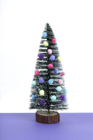 Foto de Árbol de navidad en miniatura decorado con mini guirnaldas y pompones como adornos. Fondo violeta y blanco. Fotografía mínima de naturaleza muerta - Imagen libre de derechos