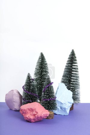 Téléchargez les photos : Forêt miniature d'arbre de Noël décorée de mini guirlandes brillantes. Fond violet. Photographie minime de nature morte - en image libre de droit