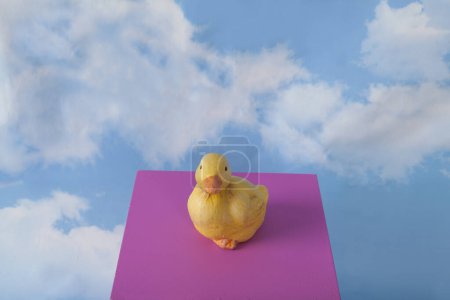 Foto de Un pato de yeso en un cubo de color rosa frente a un cielo azul con nublas.Fotografía mínima de naturalezas muertas - Imagen libre de derechos
