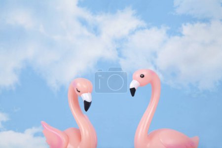 Photo for A pair of pink plastic swans against a background of blue summer sky with white clouds. Vivid color and minimal pop art photography - Royalty Free Image