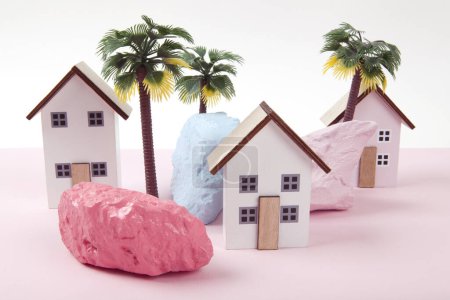 Modell von Miniatur-Strandhäusern, die ein Feriendorf in einer Harmonie von Rosa darstellen, umgeben von Palmen und Felsen, die in verschiedenen Farben bemalt sind. Leuchtende Farben und minimale Pop-Art-Fotografie