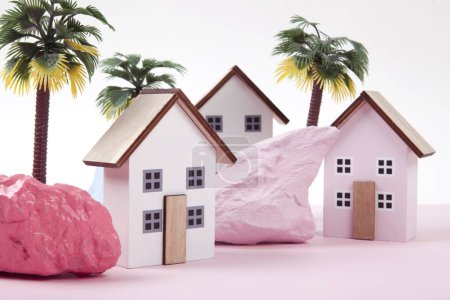model of miniature beach houses representing a vacation village in a harmony of pink surrounded by palm trees and rocks painted in different colors. Bright colors and minimal pop art photography