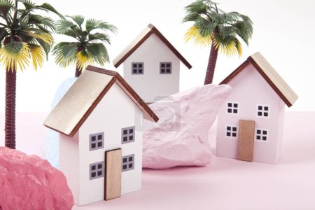 Modell von Miniatur-Strandhäusern, die ein Feriendorf in einer Harmonie von Rosa darstellen, umgeben von Palmen und Felsen, die in verschiedenen Farben bemalt sind. Leuchtende Farben und minimale Pop-Art-Fotografie