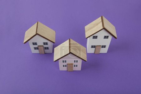 Téléchargez les photos : Un groupe de 3 maisons miniatures alignées sur un fond violet vif. Couleurs vives et photographie pop art minimale - en image libre de droit