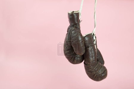 Téléchargez les photos : Une paire de vieux gants de boxe accrochés devant un fond rose bonbon. Photographie de nature morte couleur minimale et excentrique - en image libre de droit