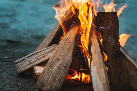 Téléchargez les photos : Une flamme de feu sur un feu de camp. Le bois empilé dans une pyramide brûle. La flamme du feu en gros plan. Une fumée blanche s'élève au-dessus du feu. Un feu de camp au barbecue. Concept touristique - en image libre de droit