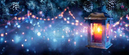 Weihnachtslaterne leuchtet in der Nacht - Kerzenschein hängende Tannenzweige mit defokussierten Schneeflocken und Bokeh-Lichtern