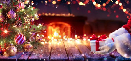 Photo pour Père Noël donner présent sous l'arbre de Noël - Boîte cadeau et ornement dans la maison intérieure avec des lumières abstraites déconcentrées la nuit - image libre de droit