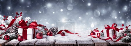 Photo for Gift On Snow In Winter White Background - Presents With Fir Branches And Red Ornaments - Royalty Free Image