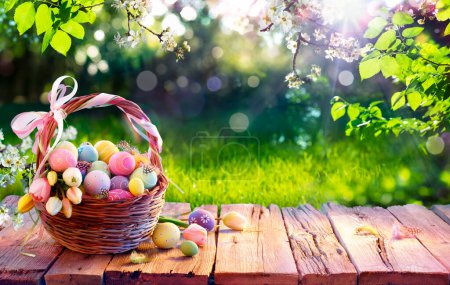 Huevos de Pascua en cesta en tabla de madera envejecida en jardín de primavera con luz solar