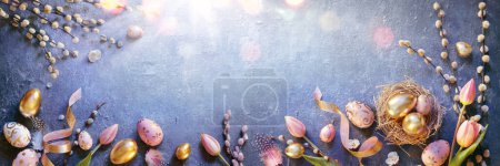 Photo for Easter - Eggs In Nest And Tulips With Golden And Pink Decorations On Blue Table With Sunshine - Royalty Free Image