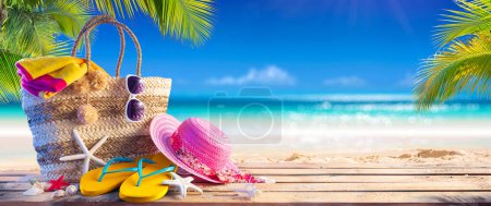 Foto de Bolsa de verano en la arena tropical - Vacaciones en la playa - Accesorios Sombrero toalla y chanclas con hojas de palma y mar azul - Imagen libre de derechos