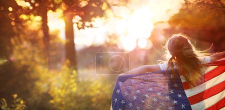Téléchargez les photos : Jour de l'indépendance - Petite fille avec drapeau américain américain - Concept de liberté - Coucher de soleil abstrait déconcentré, effet de fusée éclairante et flou de mouvement - en image libre de droit