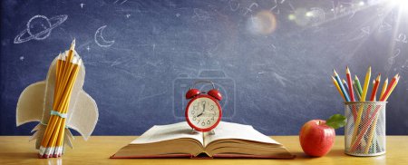 Foto de Volver a la escuela - Reloj despertador en el libro con cohete y lápices de colores con pizarra - Imagen libre de derechos