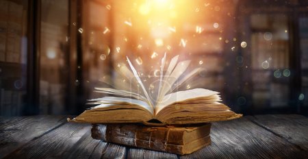 Photo for Old Book With Magic Lights And Bright Letters On Aged Table In Defocused Library - Royalty Free Image