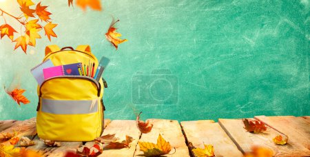 Photo for Schoolbag On Table With Stationary And Leaves - Backpack For Back To School Concept - Royalty Free Image