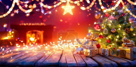 Téléchargez les photos : Présent sous l'arbre de Noël avec guirlandes à l'intérieur de la maison avec cheminée et étoile - lumières abstraites déconcentrées - en image libre de droit