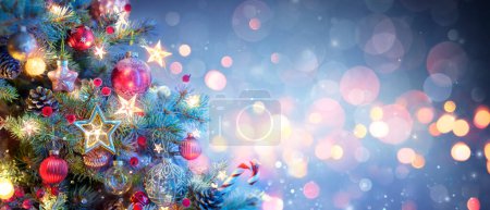 Téléchargez les photos : Arbre de Noël avec des ornements en bleu Baubles suspendus sur les branches de sapin avec scintillement et lumières Bokeh en arrière-plan abstrait déconcentré - en image libre de droit