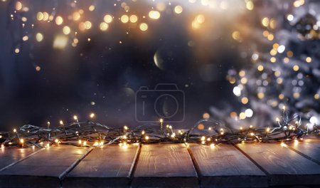 Téléchargez les photos : Noël - Lumière de corde déconcentrée sur la table en bois rustique dans la nuit avec arbre abstrait - en image libre de droit