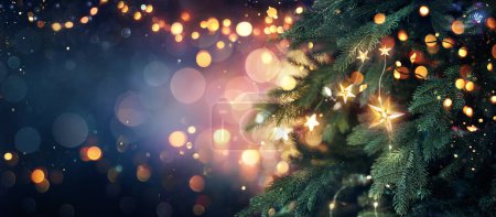 Téléchargez les photos : Arbre de Noël avec des lumières en bleu étoiles suspendues sur les branches de sapin avec scintillement et Bokeh en arrière-plan abstrait déconcentré - en image libre de droit