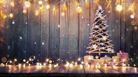 Téléchargez les photos : Décoration de Noël - Arbre en bois sur la table avec lumières rustiques et neige déconcentrée abstraite - en image libre de droit