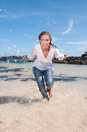 Photo for Wet young woman in clothes on the seashore in spring or summer under a blue sky - Royalty Free Image