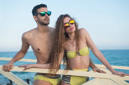 Téléchargez les photos : Jeune couple en maillot de bain sous le soleil de l'après-midi dans une zone côtière - en image libre de droit