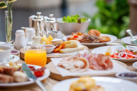 Foto de Table full of various fresh food in luxury modern restaurant. Delicious dishes, cold cuts, salmon, omelette, pastries, juices, cheese. Delicious and lavish breakfast or morning meal in high-end hotel - Imagen libre de derechos