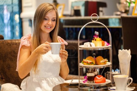 Frau in elegantem Kleid genießt englisches Frühstück Nachmittagstee im modernen Restaurant. Mädchen essen leckeres süßes Essen. Kuchen, Sandwiches und Macarons auf dem High Tea Stand.