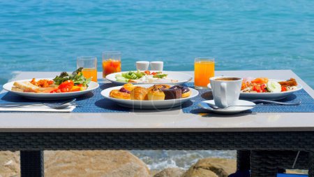 Delicioso desayuno en la costa, rodeado de las impresionantes vistas de la playa. Variedad de comida fresca en mesa fija en un restaurante de lujo junto al mar.