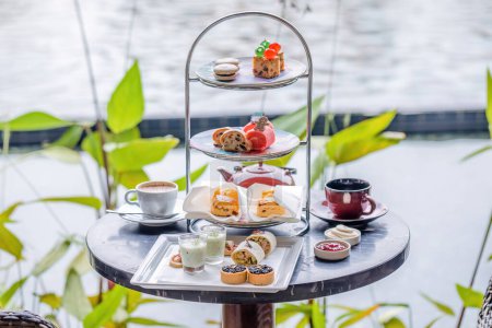 Afternoon tea stand in outdoor luxury restaurant with pond backdrop. Elegant and traditional British treat, featuring high tea, sandwiches, and sweets. Christmas style.