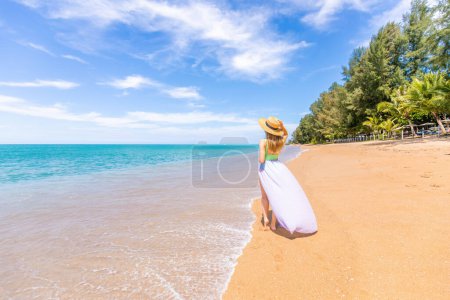 Téléchargez les photos : Voyageuse en maillot de bain aime les vacances à la plage tropicale. Mode de vie estival d'une jeune fille assez heureuse marchant sur la côte de l'océan. Plage tropicale avec eau claire. Vacances en Asie, Thaïlande - en image libre de droit