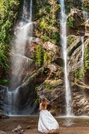 Téléchargez les photos : Femme habillée par une cascade tropicale. Beauté de la nature, voyage et aventure dans la forêt tropicale indonésienne luxuriante. Scène, sauvage et rafraîchissante. Vue arrière. - en image libre de droit