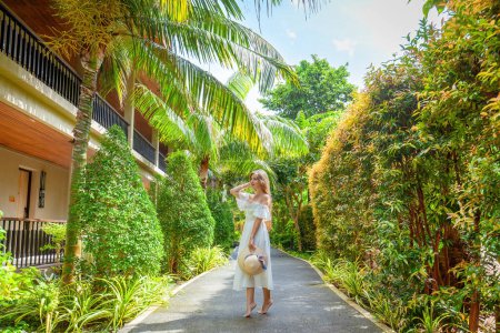 Téléchargez les photos : Magnifique femme en robe blanche profite d'une promenade tranquille dans un paradis tropical. Concept de détente et de sérénité dans un resort de luxe. - en image libre de droit
