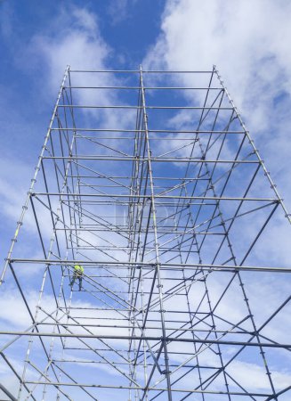 Photo for Unidentified worker at height dismantling a scaffolding tower. Blue cloudy sky on background - Royalty Free Image
