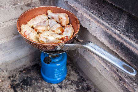 Photo for Spanish outdoor meal. Freshly chicken wings frying on a pan in camping gas stove - Royalty Free Image