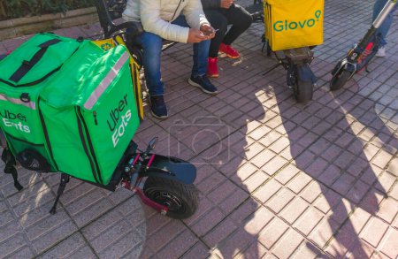 Photo for Caceres, Spain - Jan 19th, 2021: Delivery service backpacks and electric kick scooters. Urban background - Royalty Free Image