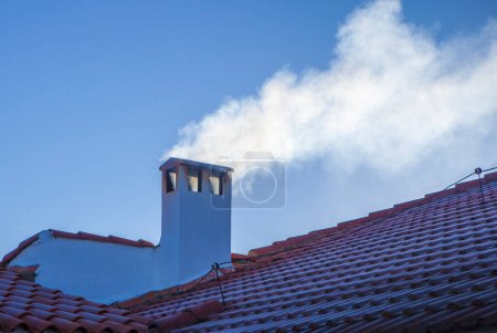 Foto de Smoky chimney on a roof covered with winter frost. blue sky background - Imagen libre de derechos