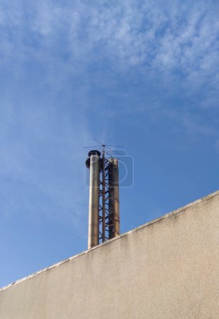 Industrieschornstein mit Vogelspitzen. Blauer Himmel Hintergrund