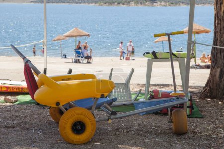 Foto de Silla de ruedas de playa cerca de la orilla del embalse lista para usar. Concepto de turismo accesible - Imagen libre de derechos