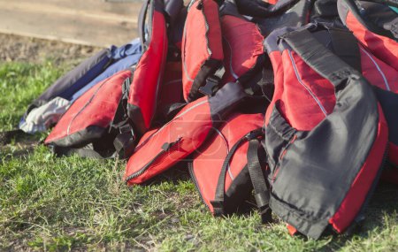 Téléchargez les photos : Des gilets de sauvetage empilés sur l'herbe. Tourisme actif sur les côtes d'eau douce concept - en image libre de droit