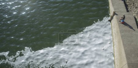 Téléchargez les photos : L'homme pêche dans une rivière polluée pleine de mousse. Poissons capturés dans les eaux polluées - en image libre de droit