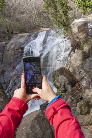 Trekker woman taking pictures with smartphone at Nogaleas waterfall, Jerte Valley, Caceres, Extremadura, Spain