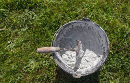 Bucket full white adhesive mortar ready for applicate. Green grass as background