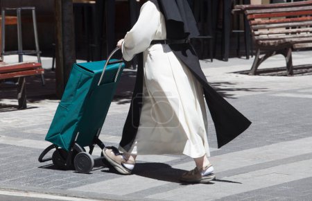 Una monja con hábitos empujando un carrito de compras en la calle. Fondo urbano