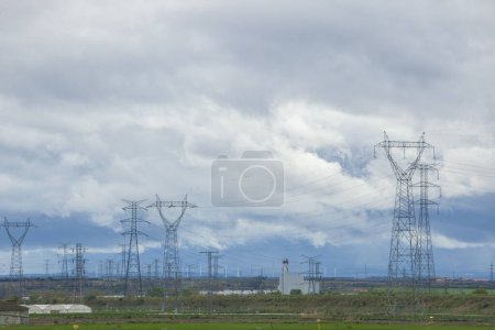 Paysage rural caché par des tours électriques, des câbles haute tension et des éoliennes. Concept d'impact environnemental des éoliennes