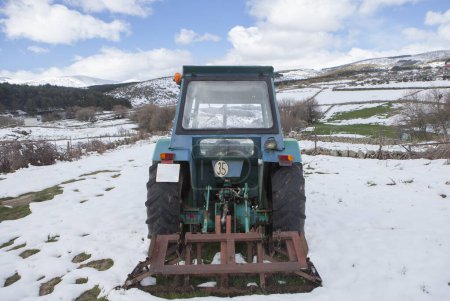 Antiguo tractor equipado con implemento aparcado en medio de un prado cubierto de nieve. Concepto agricultura de montaña